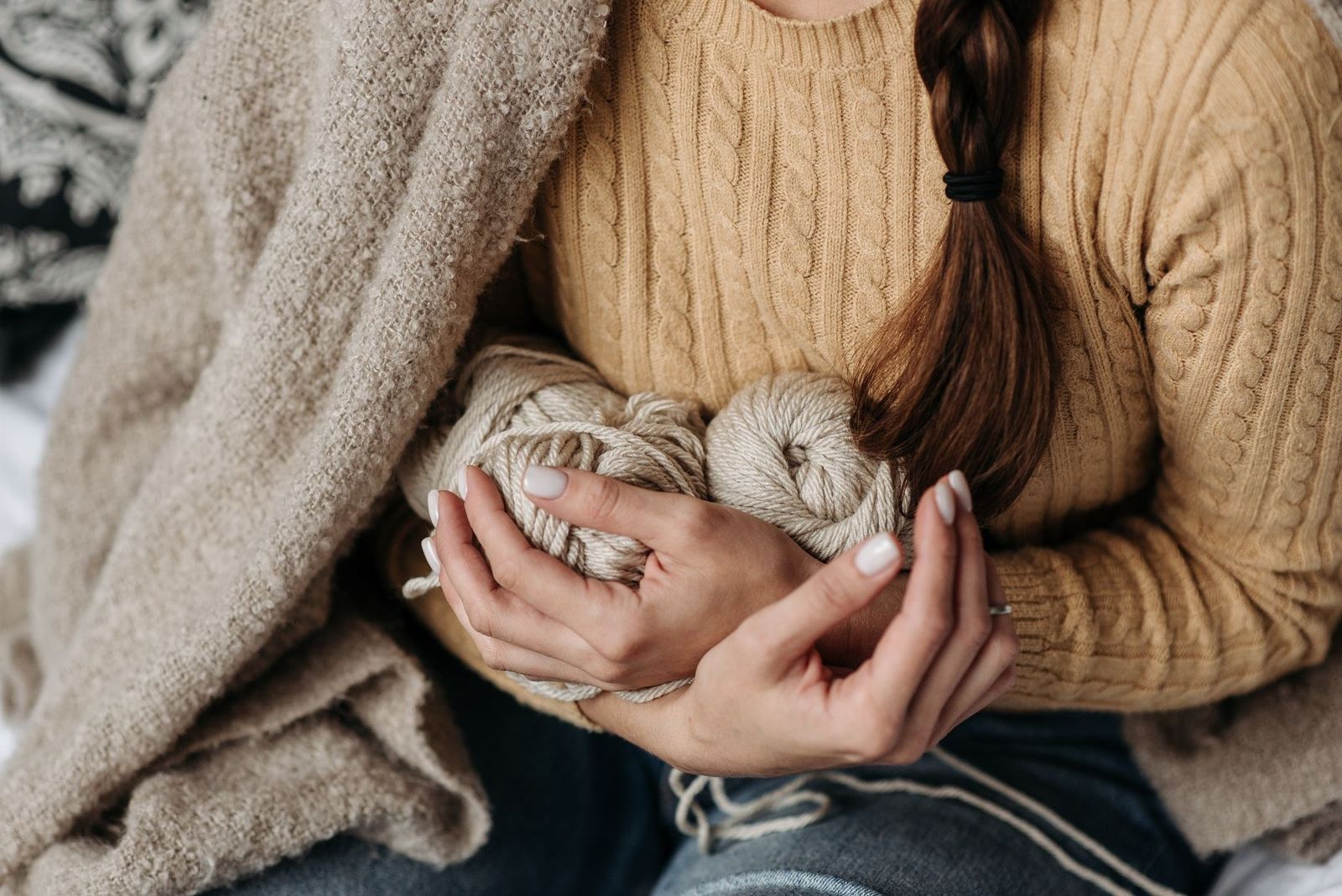 Manos sosteniendo ovillos de lana envueltas en un sweater tejido